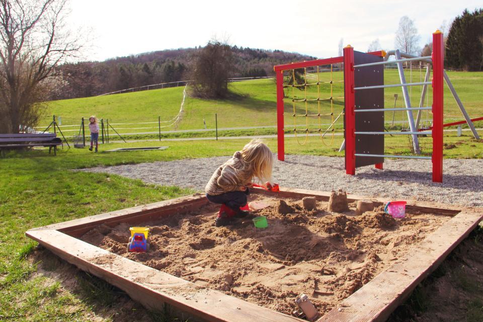 Ein kleines Mädchen spielt im Sandkasten, im Hintergrund ist ein Klettergerüst zu sehen
