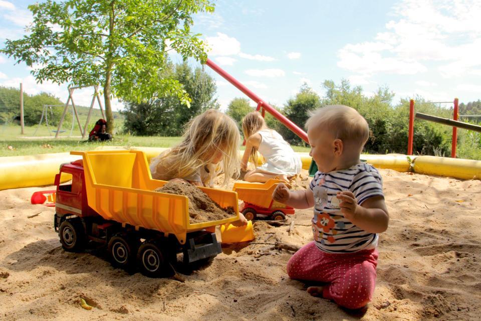 Drei Kleinkinder spielen im Sandkasten mit Kinderspielzeug, Baustellenfahrzeugen