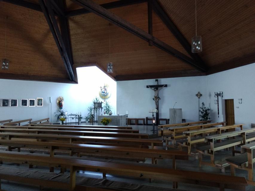 Sowohl die Bänke, als auch die Decke der Kirche sind aus Holz gebaut. Das Innere der Kirche ist dezent mit ein paar Grünpflanzen, einem Jesukreuz, Altar und Kerzen geschmückt.
                 title=