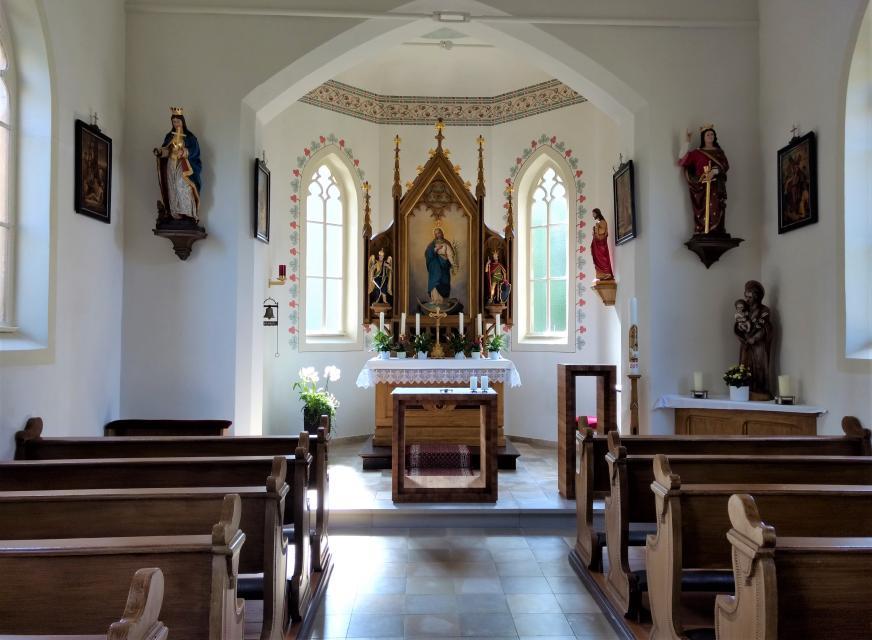 Der Innenraum ist mit hölzernen Bänken ausgestattet. Der Altarraum zeigt ein Bild, auf welchem Gott das Jesuskind in seinen Armen hält.