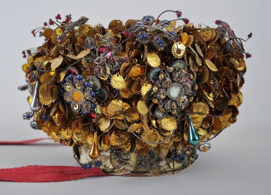 Eine aufwendig gearbeitete Krone, die aus vielen runden goldenen Blättchen und bunten Steinen besteht.