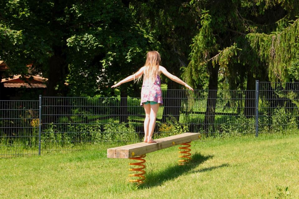 Ein Mädchen balanciert auf einem Holzbalken, der auf elastischen Sprungfedern befestigt ist;