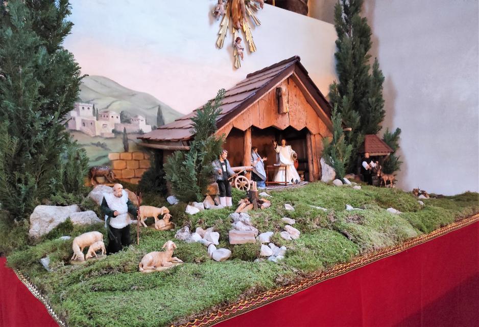 Die Krippe erhebt sich auf dem höchsten Punkt einer Mooslandschaft. Neben Engel und Maria im Hintergrund stehen Schafe und ein Hirte im Vordergrund.