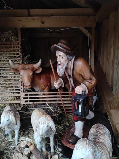Ein Hirte mit einer Lampe und einem Stock in der Hand steht bei Schafen und dem Ochs im Stall.