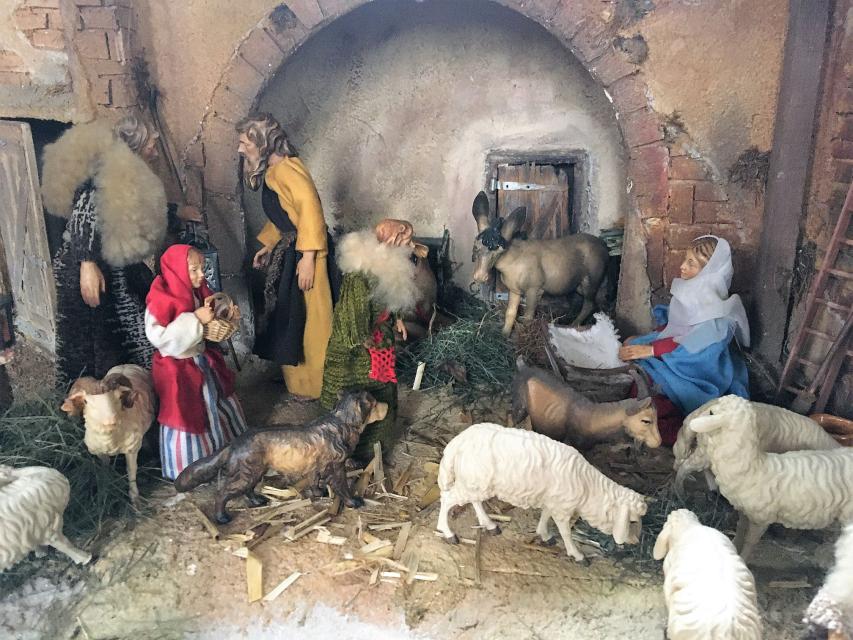 Im Stall mit Rundbogen sind vor den Figuren Maria, Josef und Hirten einige Schafe versammelt.