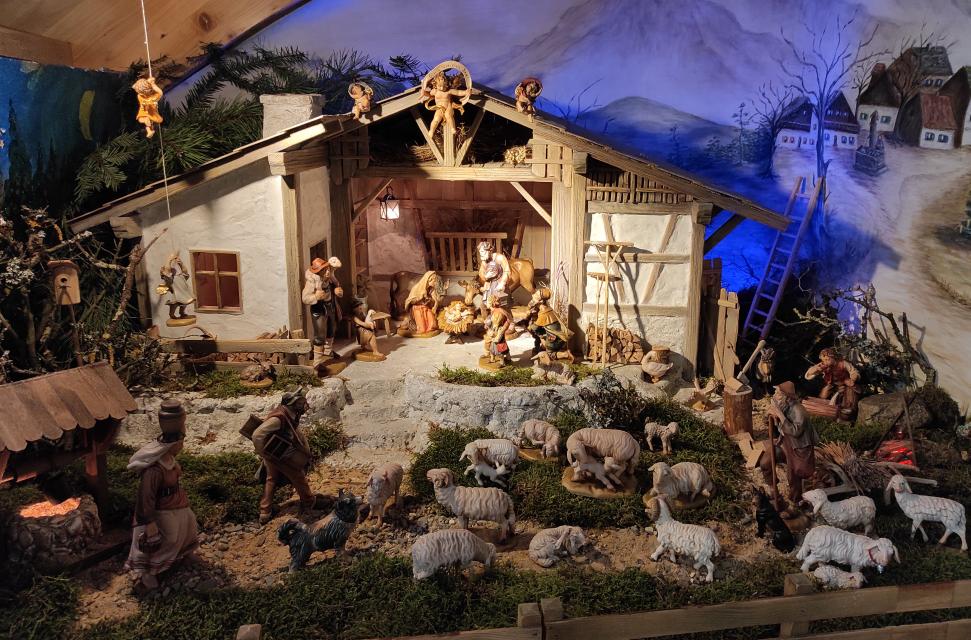 Oberbayerische Krippendarstellung mit Josef, Maria und Jesuskind. Vor der Krippe stehen weitere Figuren und Schafe im Moos.