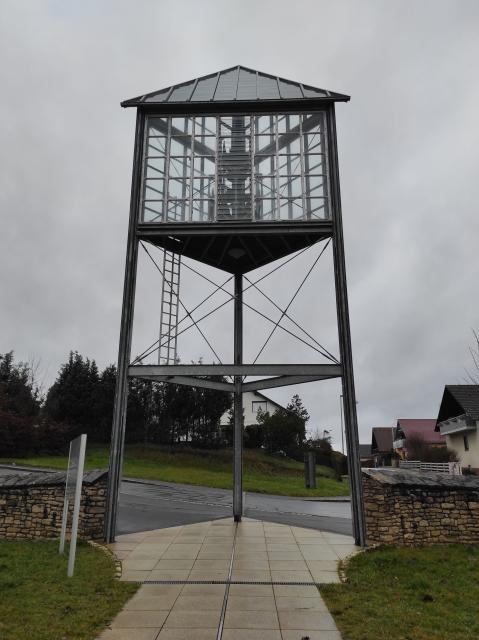 Der Glockenturm besteht aus einem Metallgestell. Die Glockenanlage ist gläsern verkleidet.
                 title=