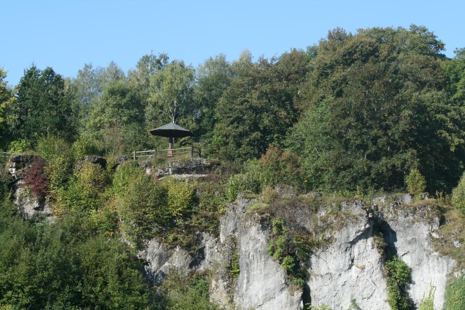 Oberhalb einer Felskante, hinter der sich Wald befindet, steht ein pilzförmiger Aussichtspavillon.