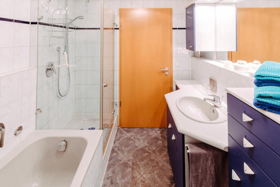 kleines Badezimmer mit Badewanne und Dusche, rechts Waschbecken und Badmöbel