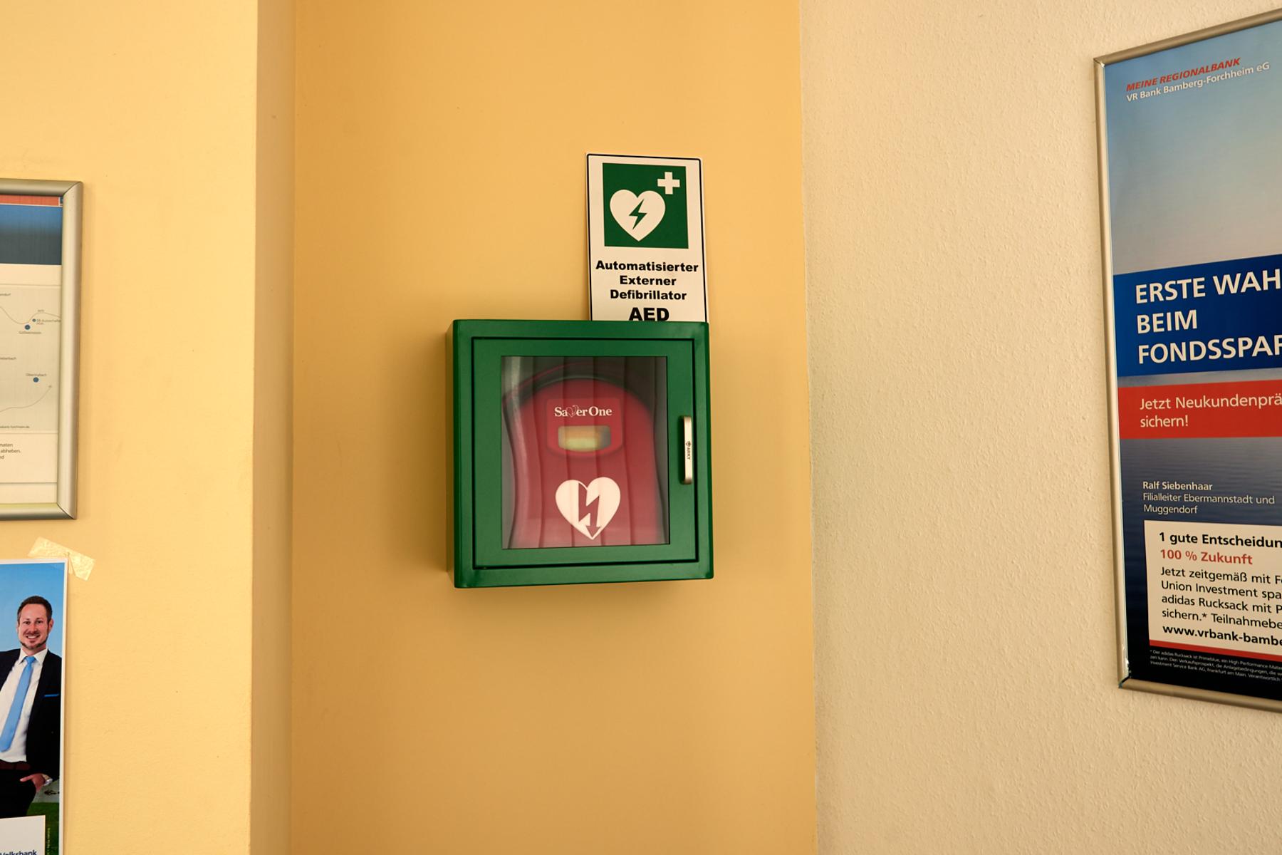 Defibrillator Muggendorf Volksbank, Nahaufnahme, im Vorraum an der linken Wand