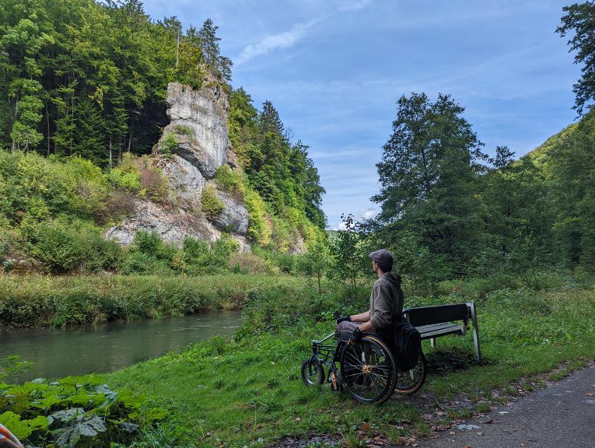 Ein Rollstuhlfahrer blickt an einem Weg auf eine Felswand.