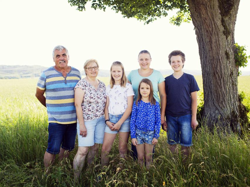 Eine Familie mit vier Kindern steht in einer Wiese unter einem Baum.
