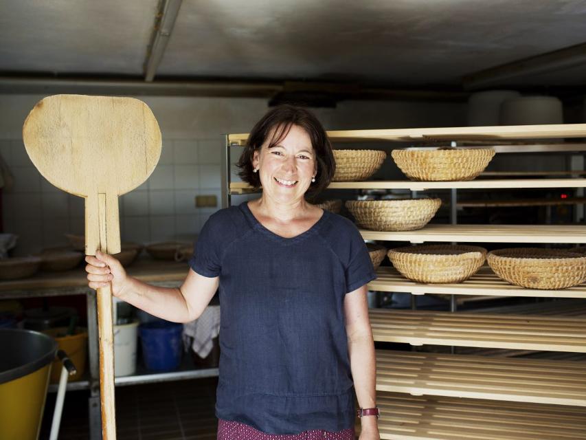 Ein Frau steht mit einem Brotschaber vor Holzofenbrot.
