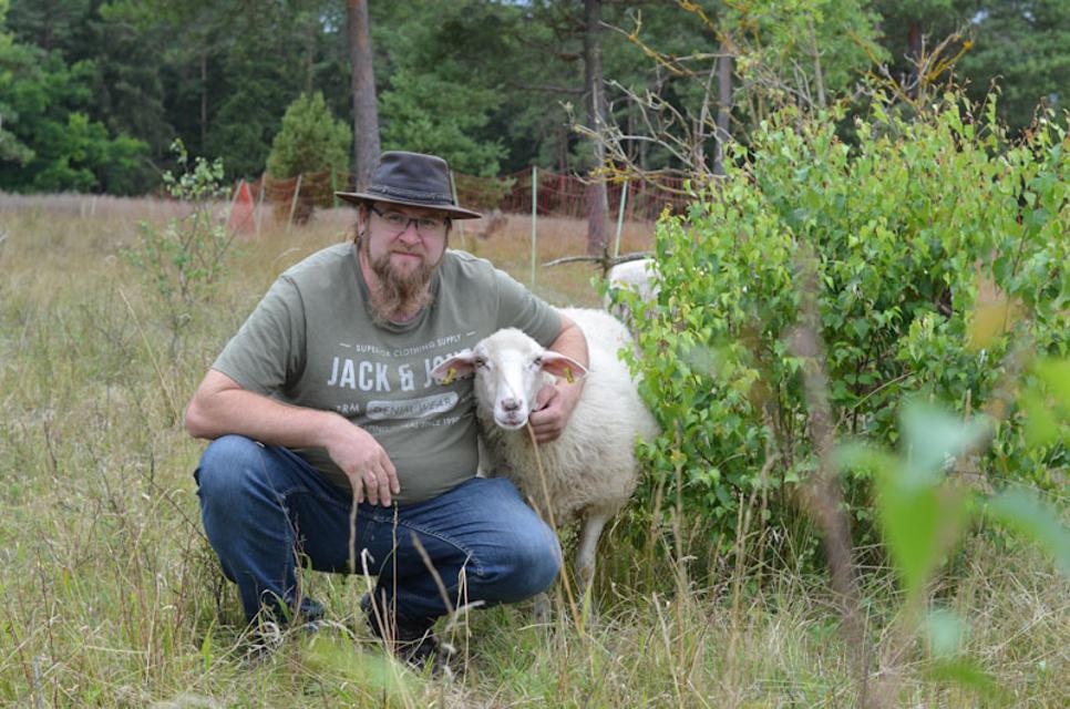 Ein Mann kniet neben einem Schaf und umarmt es.