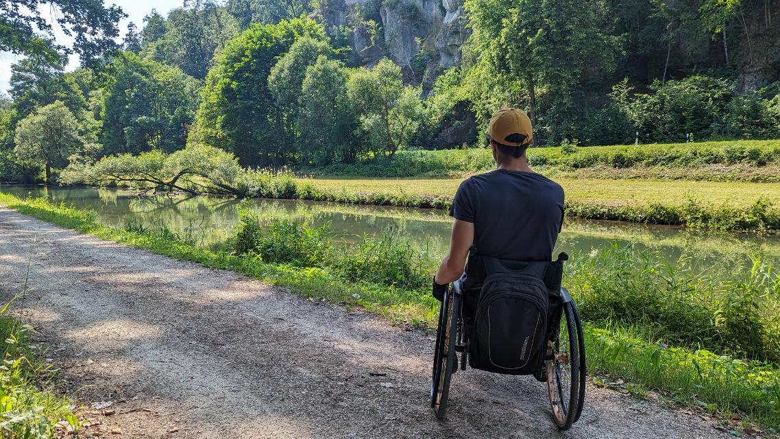 Ein Mann im Rollstuhl auf einem Schotterweg neben einem Bach.