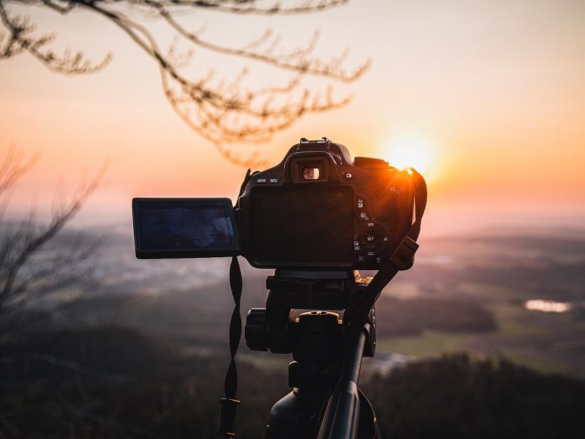 Eine Fotokamera steht auf einem Stativ in der Abendsonne.