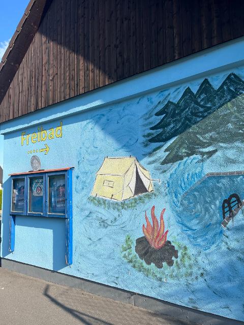 Das Bild zeigt eine bemalte Hausfront mit Schwimm- und Zeltplatzsymbolen.