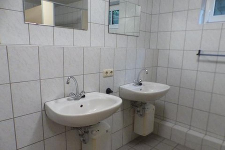 Das Bild zeigt einen gefliesten Raum mit zwei Waschbecken, über den Waschbecken sind Spiegel montiert.