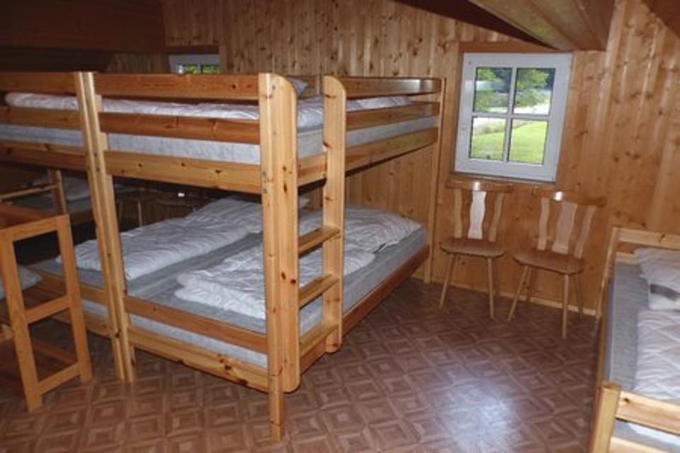 Das Bild zeigt hölzernes Etagenbett mit vier Schlafplätzen sowie zwei Holzstühle und ein weiteres Holzbett.