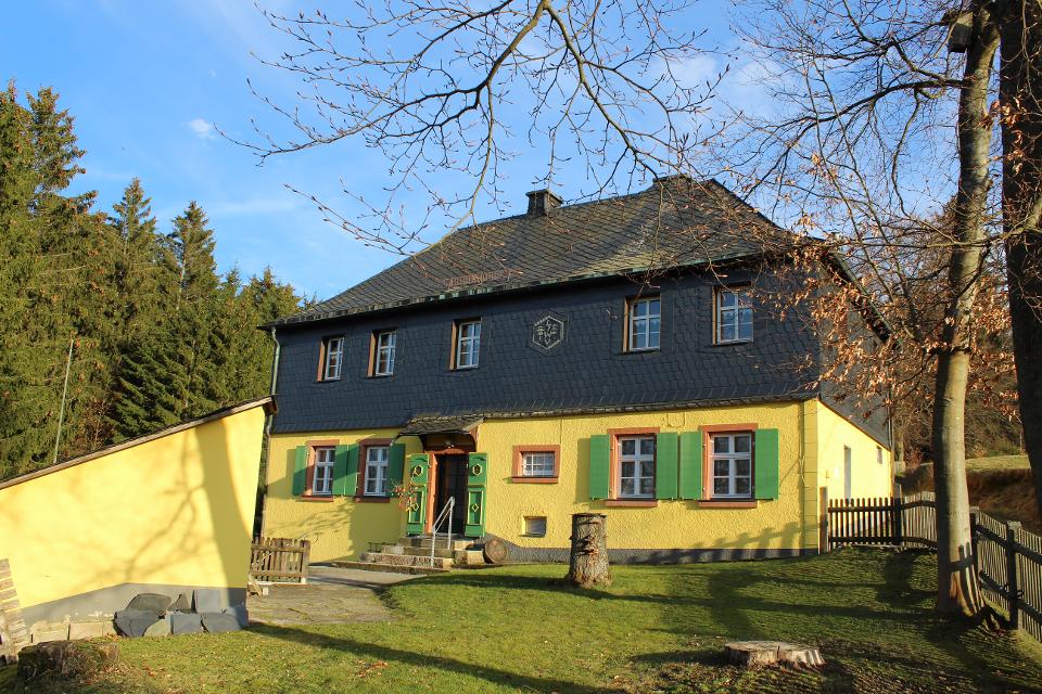 Das Bild zeigt das Wanderheim Gerlaser Forsthaus, ein gelb gestrichenes Gebäude mit Schieferverkleidung im ersten Stock.