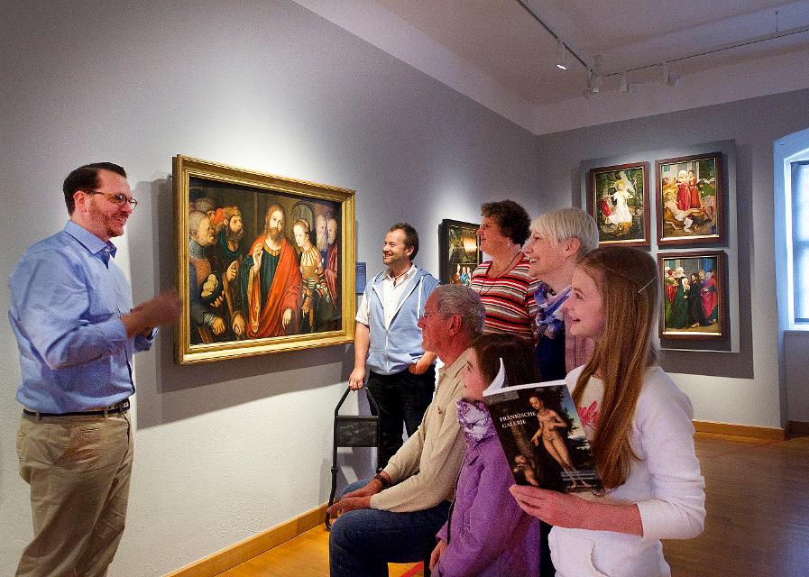 Ein Gruppe Menschen steht vor einem Bild des Künstlers Lucas-Cranach und hört einem Museumsführer zu.