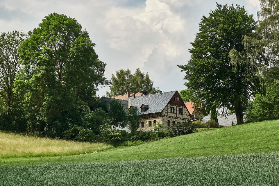 Das Bild zeigt ein Fachwerkhaus, neben dem links und rechts Laubbäume stehen.