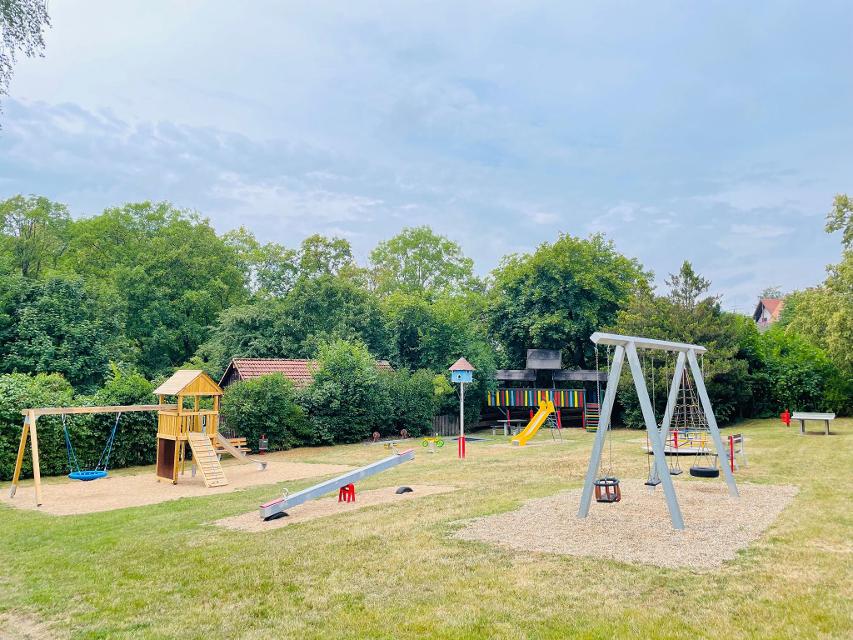 Das Bild zeigt den Spielplatz in Guttenberg. Man sieht diverse Spielmöglichkeiten: Wippe, Federwippe, Rutsche, Schaukel, Kletter- und Spielturm, Rutsche, Karussell.