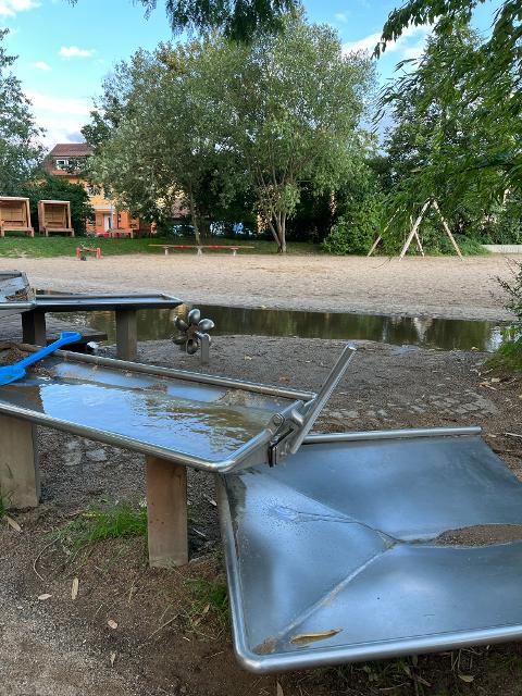 Das Bild zeigt diverse Wasserspielelemente beim Wasserspielbereich am Spielplatz im ehemaligen Landesgartenschaugelände in Kronach. Es gibt diverse Staudämme, Wasserräder & Co.