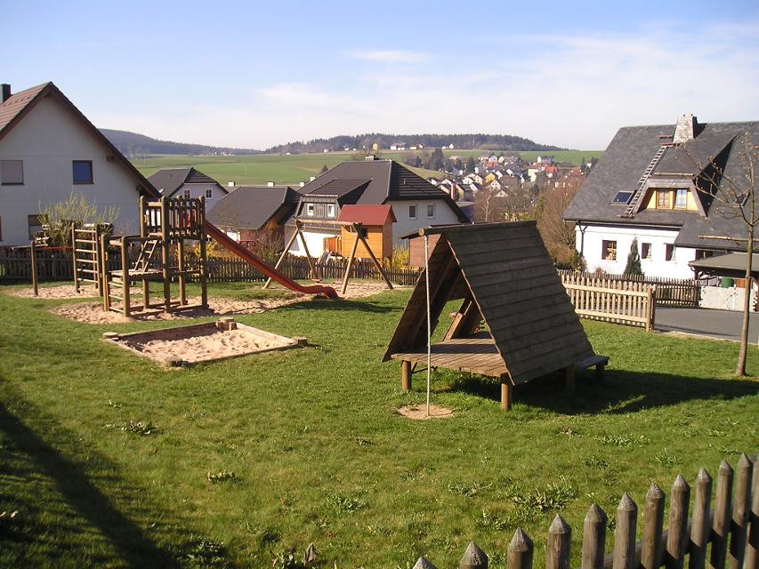 Das Bild zeigt den Spielplatz in Geroldsgrün., Es gibt eine Schaukel, einen Kletterturm mit Rutsche, diverse Turngeräte und einen Sandkasten.