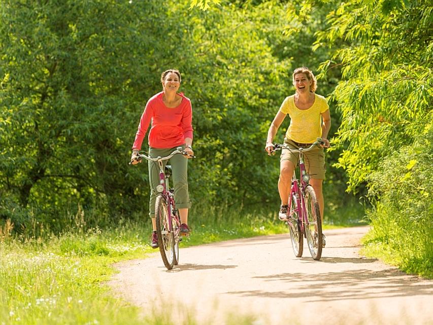 Zwei sommerlich gekleidete Frauen fahren auf lilafarbenen Fahrrädern