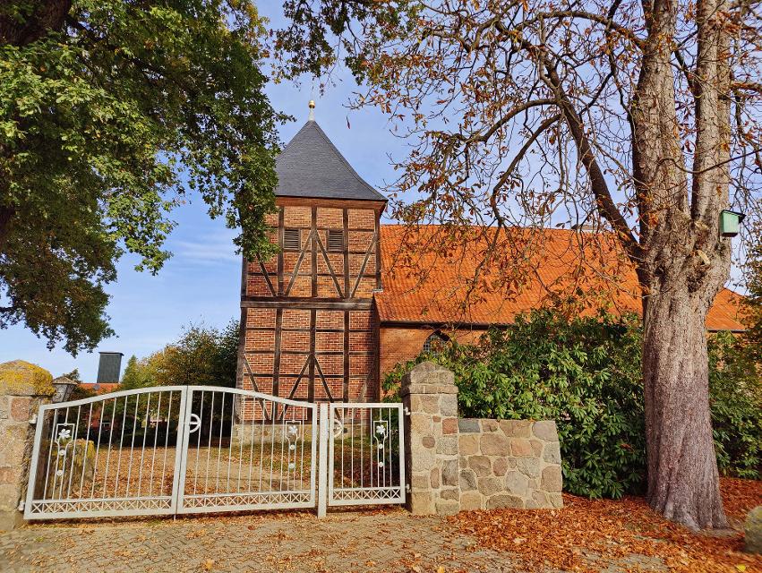 Eisernes Eingangstor zur Feldsteinkirche in Bienenbüttel OT Wichmannsburg, mit Steinmauer und Bäume an den Seiten, Kirche im Hintergrund