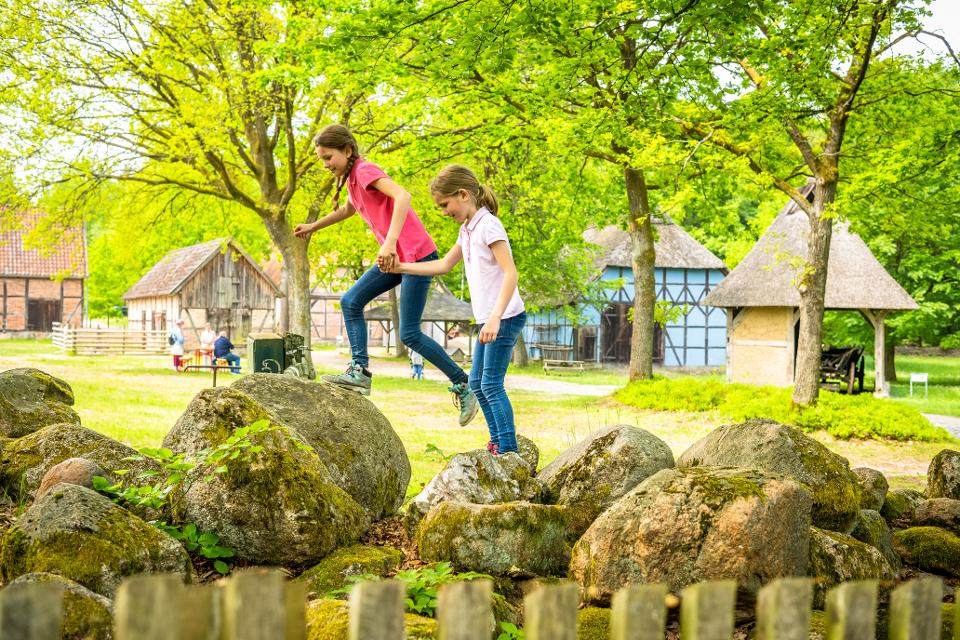 Zwei Mädchen spielen auf Steinen im Museumsdorf Hösseringen