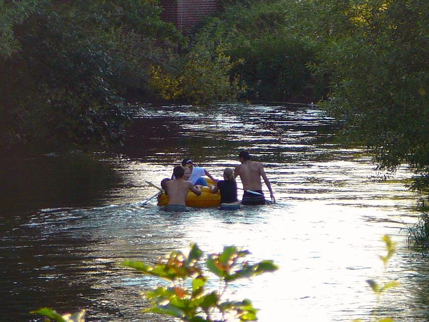 Eine Gruppe Jugendliche und junge Erwachsene badet mit einem großen gelben Schwimmreifen im knietiefen Wasser der Ilmenau