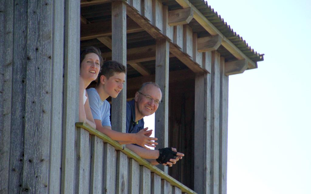 Eine Familie (Mutter, jugendlicher Sohn und Vater) blickt aus einer hölzernen Aussichtsplattform