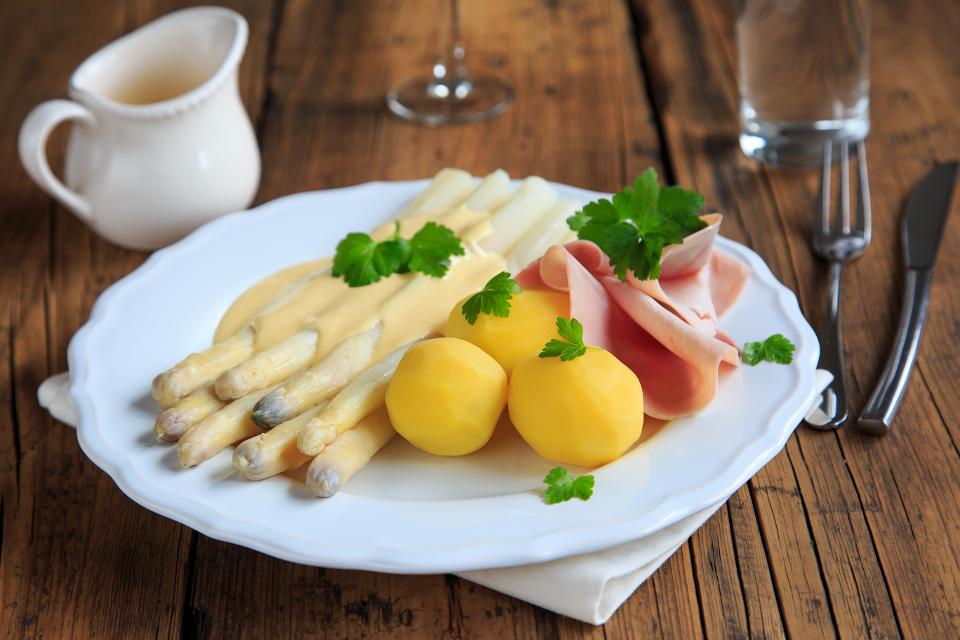 Spargel mit Schinken und Kartoffeln auf einem weißen Teller auf einem Holztisch