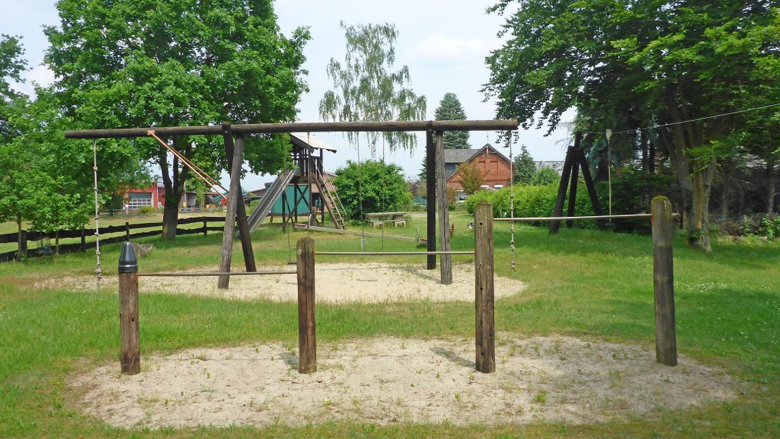 Rechstangen, Schaukeln, Klettertaue, Rutsche, Seilbahn und andere Spielgeräte auf dem von Bäumen eingefassten Spielplatz in Grabau
