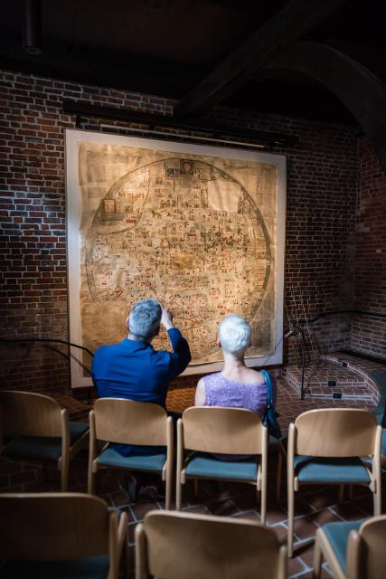 Zwei Besucher auf Stühlen sehen sich die Ebstorfer Weltkarte an