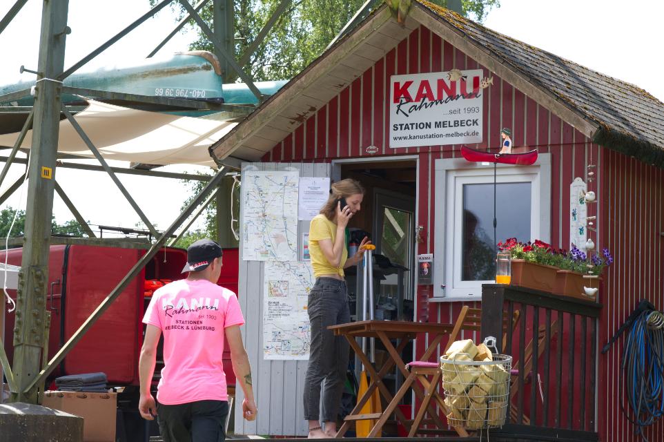 Station Kanu Rahmann mit rotem Häuschen, ein Mann im pinken T-Shirt geht rein, eine Frau telefoniert