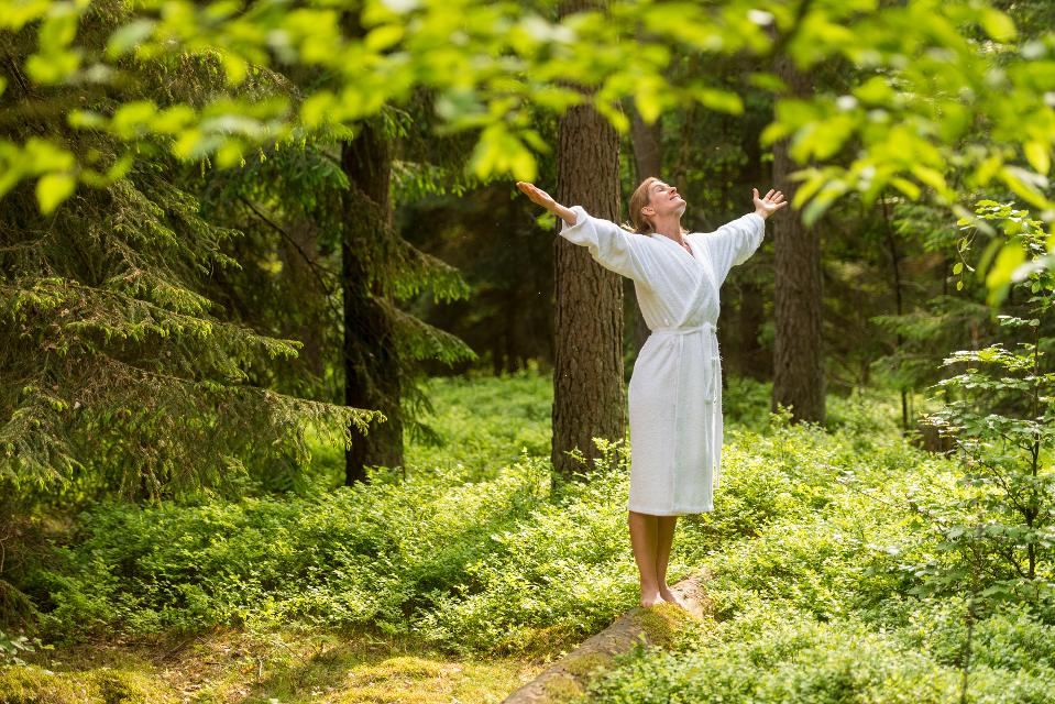 Frau im weißen Bademantel im Wald, streckt die Arme aus