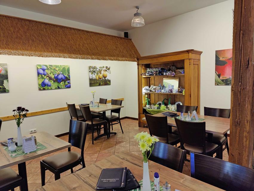 Dunkle Stühle und Holztische im Restaurant der Obstscheune, Blumendeko auf den Tischen, Holzvitrine im Hintergrund, Bilder mit Obst an den Wänden