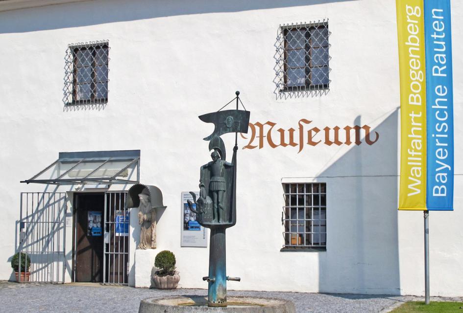 Der Eingang zum Kreismuseum auf dem Bogenberg. Vor dem Gebäude steht der Floriansbrunnen und eine gelb blaue Fahne.