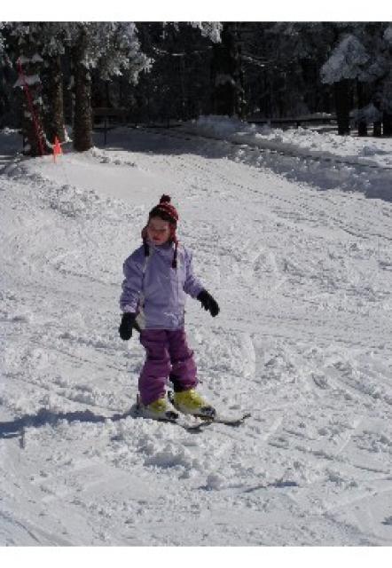 Eine Pulverschneepiste an einem sonnigen Wintertag. Ein Kind fährt auf Skiern, aber ohne Stöcke, langsam talwärts.