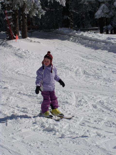 Ein Kleinkind fährt an einem sonnigen Wintertag mit Skiern auf der Piste langsam talwärts.