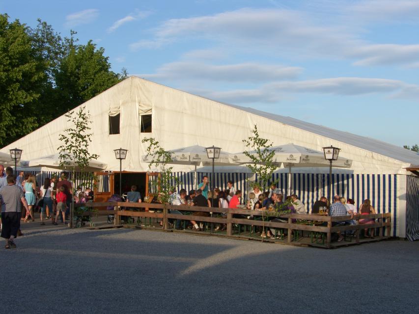 Der Biergarten vor dem Bierzelt ist bereits gut besucht, weitere Gäste gehen in das Zelt.