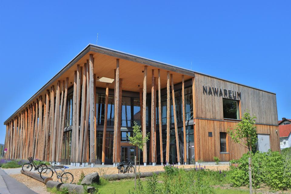 Außenansicht vom Mitmachmuseum Nawareum. Die Konstruktion besteht großteils aus Holz. Die auffällige Fassade wird von naturbelassenen Baumstämmen gestützt.