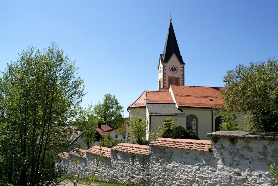 Hinter der Friedhofsmauer liegt die Pfarrkirche Sankt Engelmar mit ihrem wuchtigen, markanten Kirchturm.