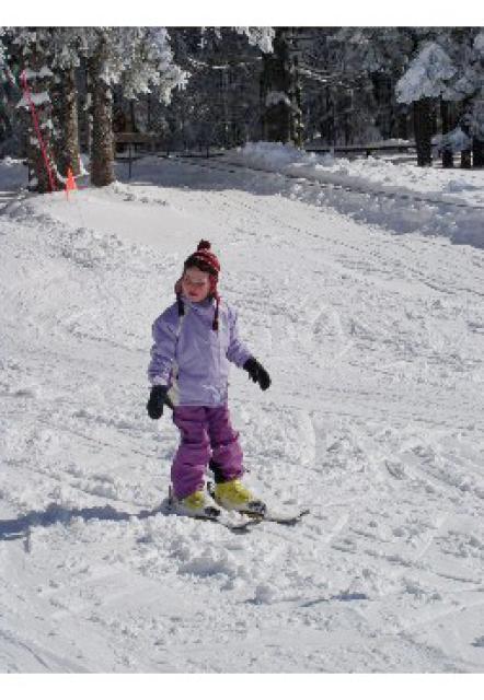 Eine Pulverschneepiste an einem sonnigen Wintertag. Ein Kind fährt auf Skiern, aber ohne Stöcke, langsam talwärts.