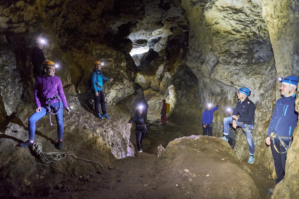 Gruppe mit Helmen, Stirnlampen und Klettergurten ausgerüstet in einer großen Höhlenhalle