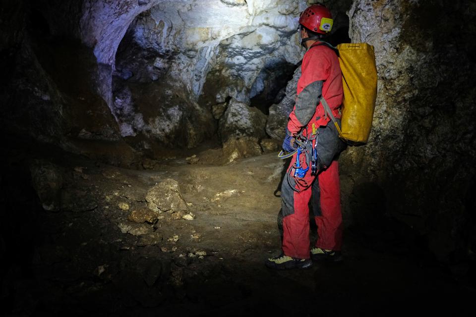 Höhlenguide mit Helm, Stirnlampe, Rucksack und Kletterausrüstung in einer kleinen Höhlenhalle