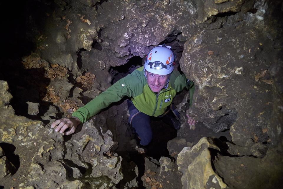 Mann mit Helm und Stirnlampe steigt durch eine schmalen Schacht in der Höhle aufwärts